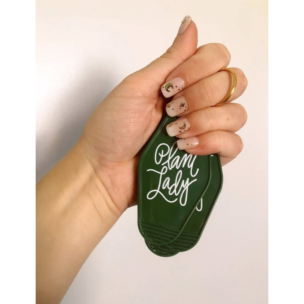 hand holding a green plant lady retro motel keychain with white letters