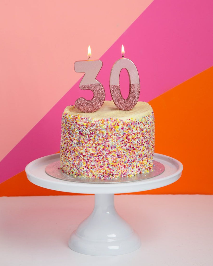 rose gold number candles with rose gold glitter on a yellow cake with multicolored sprinkles